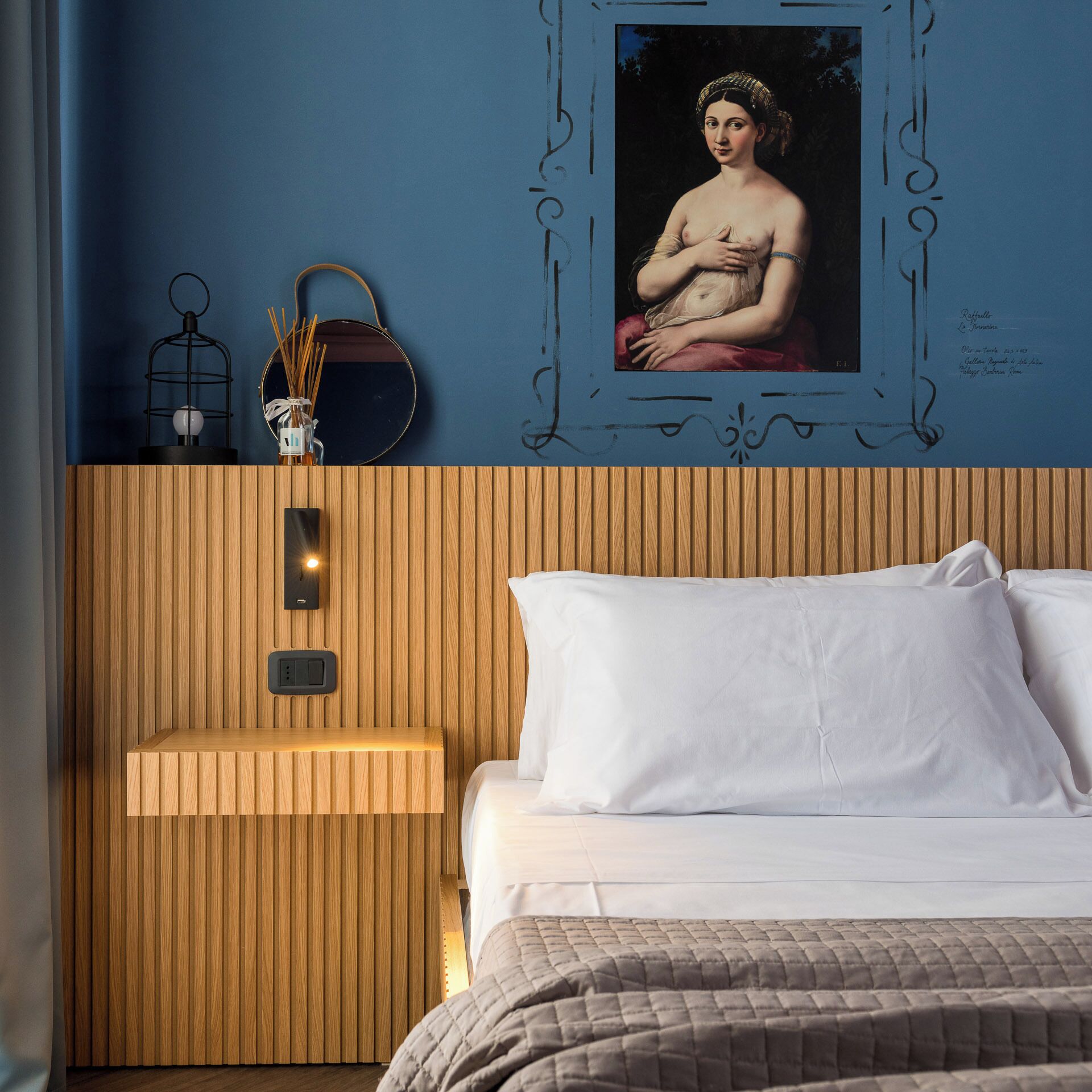 A bedroom with a wooden headboard, a bedside table with a lamp, and a framed painting on the wall.