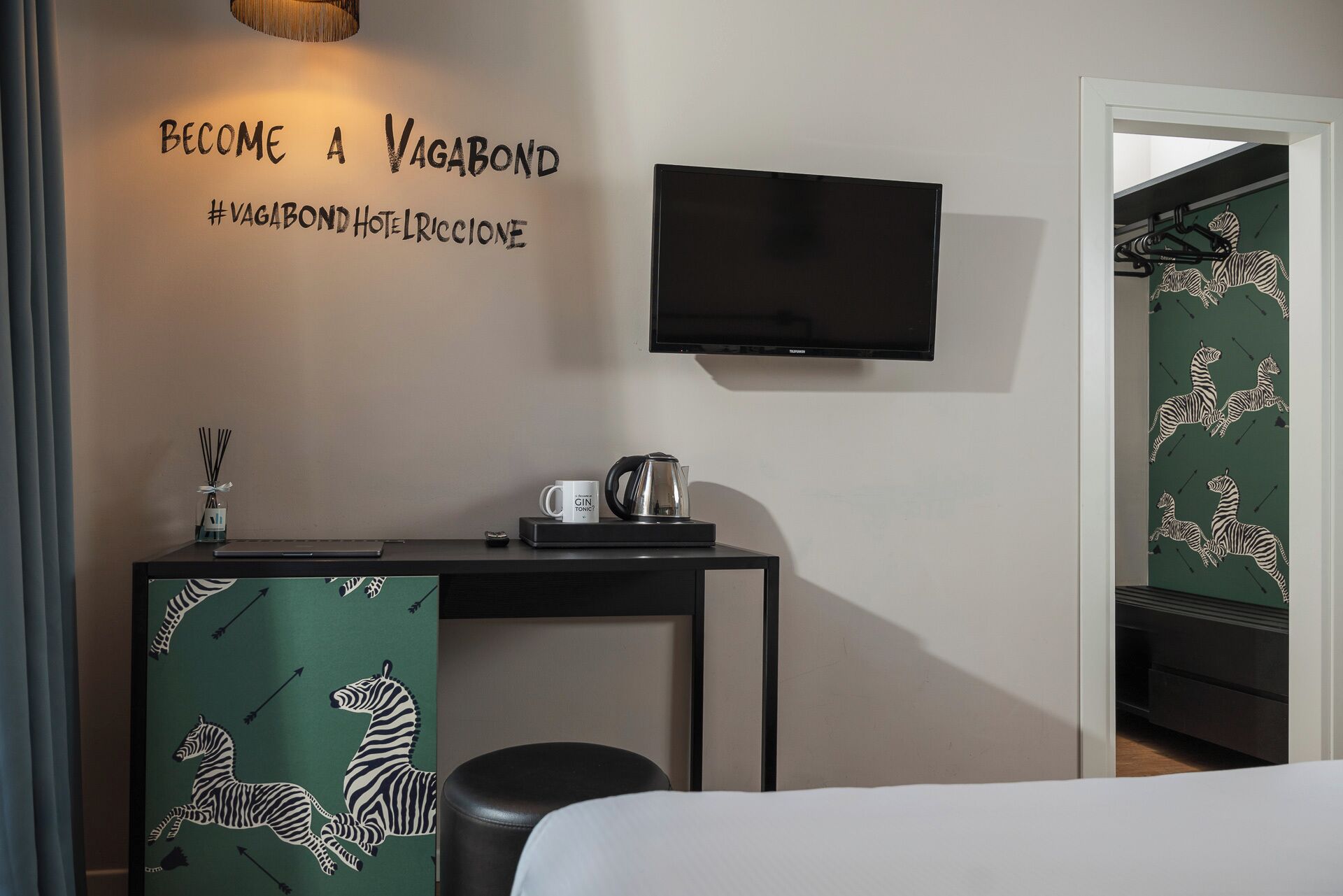 Camera d'albergo con un letto, una scrivania con bollitore e tazza, televisione e una parete a tema zebra.