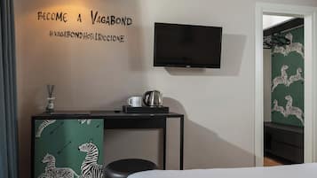 Camera d'albergo con un letto, una scrivania con bollitore e tazza, televisione e una parete a tema zebra.