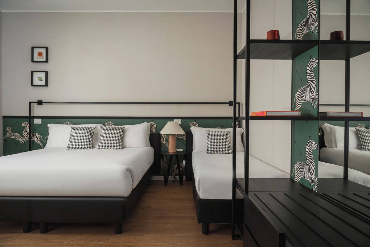 Ein modernes Hotelzimmer mit einem Bett, Nachttischen, einer Lampe und einem Bücherregal.
