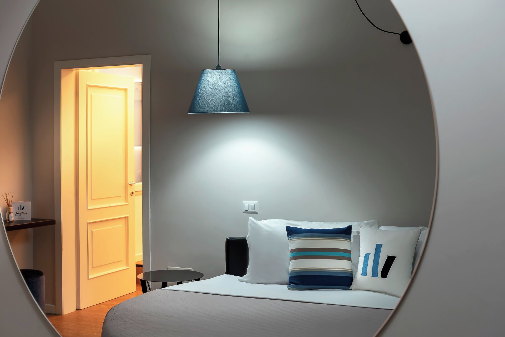 A bedroom with a bed, bedside table, lamp, and a door leading to another room.