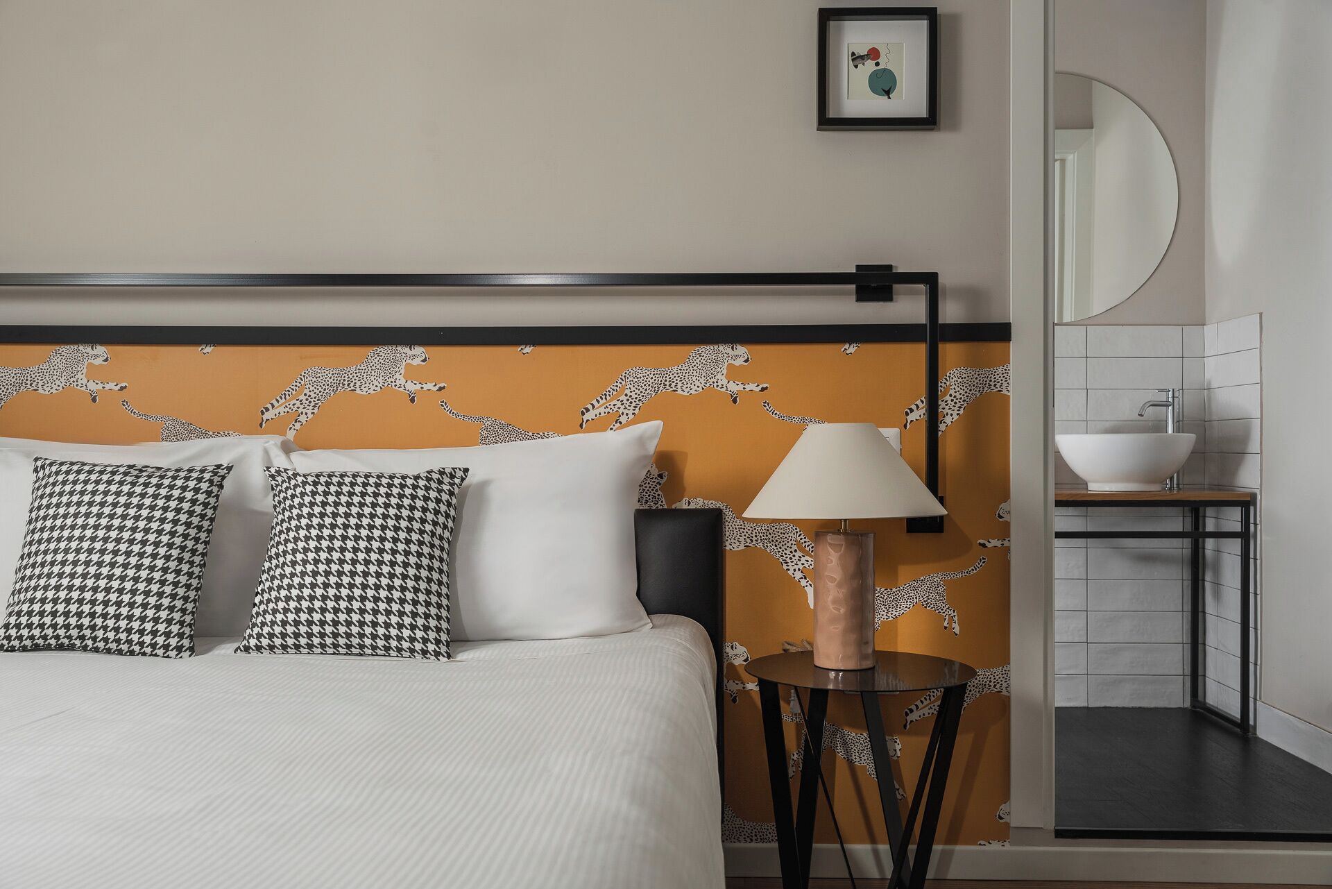 A neatly made bed with patterned pillows, a bedside lamp, and a wall with leopard print wallpaper.