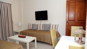 A room with a bed, a TV mounted on the wall, a small table, and a chair. - Volanakis Apartments (Malevizi)