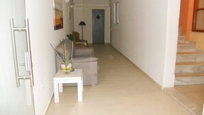 A hallway with a staircase leading to a door, a small table with a plant, and a chair. - Volanakis Apartments (Malevizi)