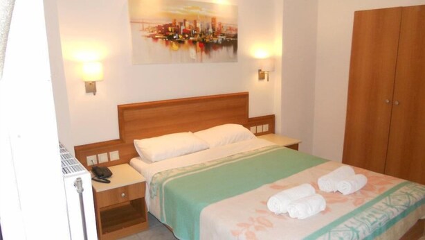 A hotel room with a bed, a nightstand, a wooden wardrobe, and a painting on the wall. - Volanakis Apartments (Malevizi)