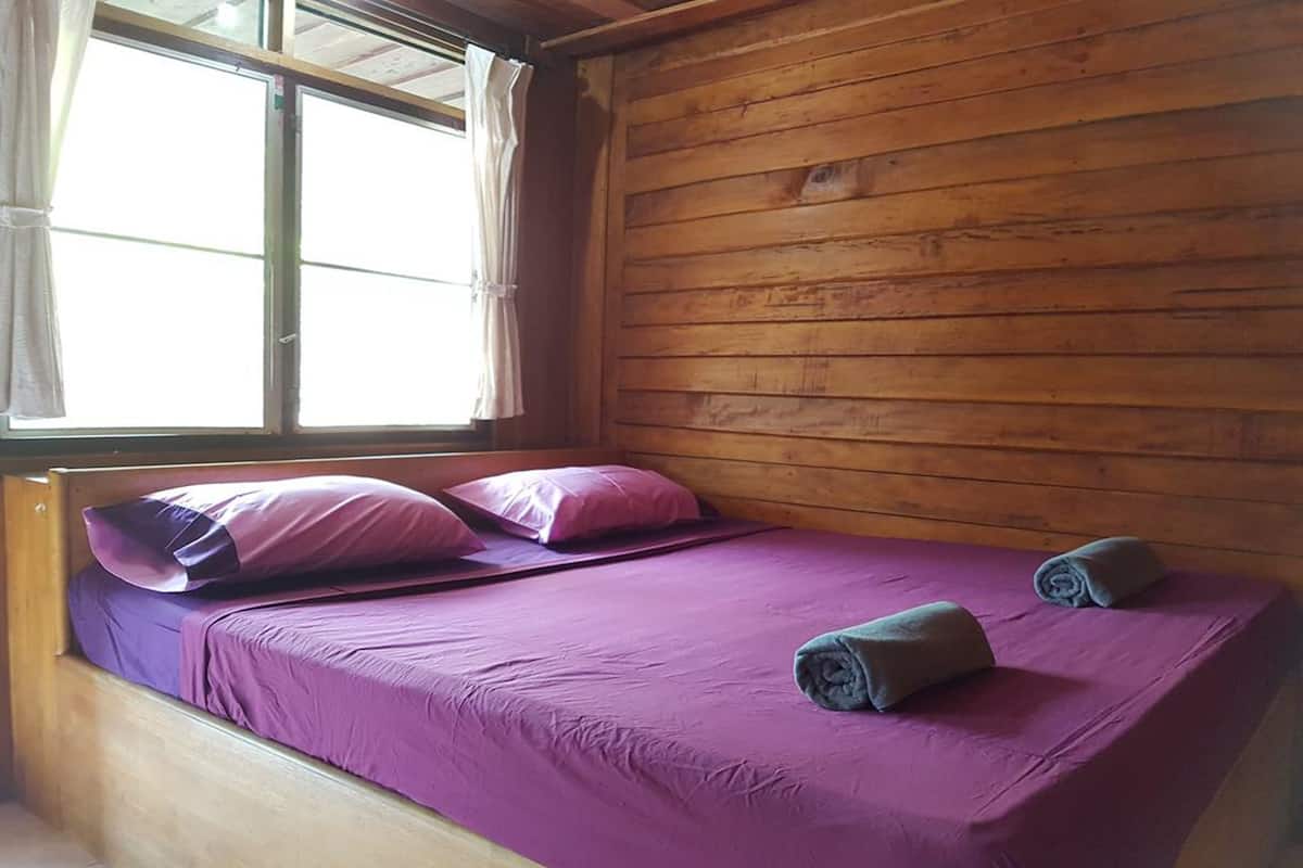 A single bed with purple bedding, a window with curtains, and wooden walls.