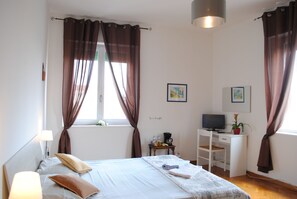 Un dormitorio con cama, escritorio, silla, lámpara y dos cuadros en la pared.