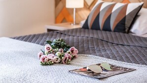 Ein ordentlich bezogenes Bett mit einer gesteppten Decke, ein Blumenstrauß und eine Sonnenbrille auf einer Zeitschrift.