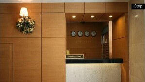 A reception desk with a sign labeled "INFORMATION," a wall-mounted clock, and a decorative floral arrangement. - L'S Hotel (Jeongseon)