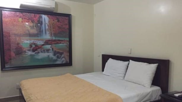 A bedroom with a bed, a painting of a waterfall, and a nightstand. - Quynh Trang Hotel (Hai Phong)