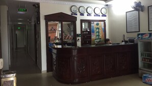 A reception area with a wooden counter, a clock above it, and a refrigerator with La Vic water bottles. - Quynh Trang Hotel (Hai Phong)