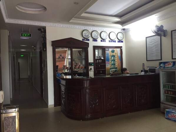 A reception area with a wooden counter, a clock above it, and a refrigerator with La Vic water bottles.