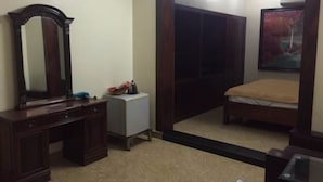 A bedroom with a wooden dresser, a bedside table, a mirror, a wardrobe, and a bed with a beige blanket. - Quynh Trang Hotel (Hai Phong)