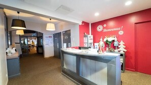 A reception area with a red wall, a welcome sign, and a counter with various items. - Hôtel Les Carrettes (Valmeinier)