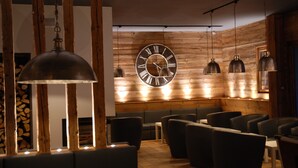 A restaurant interior with wooden walls, a large wall clock, hanging pendant lights, and modern seating. - Hôtel Les Carrettes (Valmeinier)