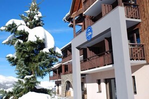 A multi-story hotel with wooden balconies and a sign indicating it is a ski resort. - Hôtel Les Carrettes (Valmeinier)