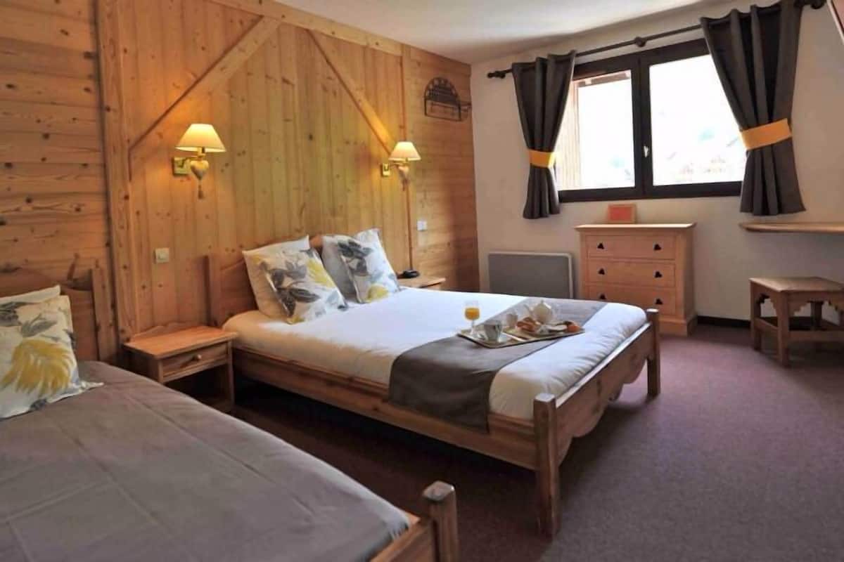 Ein Zimmer mit Holzboden, einem Bett, Nachttischen, einem Schminktisch und einem Fenster mit Vorhängen.