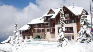 A multi-story lodge with a ski slope in the background. - Hôtel Les Carrettes (Valmeinier)