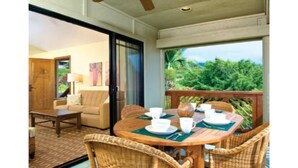 A dining area with wicker chairs and a table set for two, a sliding glass door leading to a room with a sofa, and a view of lush greenery outside. - Ironman 2026! Easy access to Ironman & everything else!  Great Rate! Sleeps 6! (Kailua-Kona)
