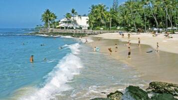 A beach with clear water, palm trees, and people swimming and sunbathing.