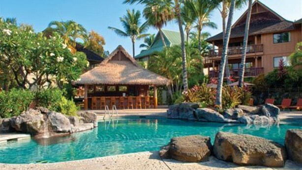 A resort pool with a thatched-roof hut, palm trees, and a building with balconies. - Ironman 2026! Easy access to Ironman & everything else!  Great Rate! Sleeps 6! (Kailua-Kona)