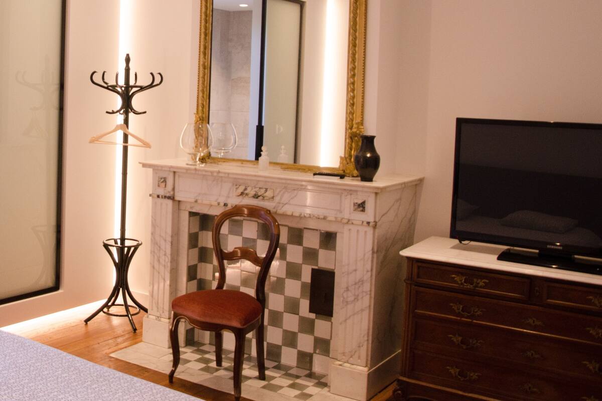 A bedroom with a large mirror, a television, a chair, a dresser, and a floor lamp.