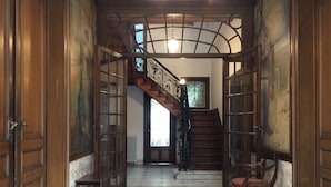 A grand hallway with a marble floor, a wooden staircase, and a large window with a view of a tree.