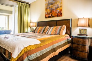 A neatly made bed with a striped quilt, a wooden headboard, and a bedside table with a lamp. - GRAND PANAMA BEACHFRONT, 1ST FLR DIRECT to BEACH. $250 SpecialSMART TV/FREE WIFI (Panama City Beach)