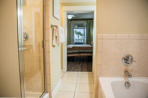 A hotel bathroom with a glass shower enclosure, a bathtub, and a view of a balcony with a bed. - GRAND PANAMA BEACHFRONT, 1ST FLR DIRECT to BEACH. $250 SpecialSMART TV/FREE WIFI (Panama City Beach)