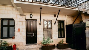 A stone building with a black door, windows, and a fire extinguisher. There are potted plants and a bench. - Arifbey Konagi Otel (Gaziantep)