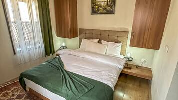 A bedroom with a bed, a nightstand, a lamp, a painting, and a wooden ceiling.