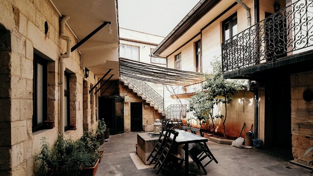 A narrow alley with a table and chairs in the center, flanked by buildings with balconies and potted plants. - Arifbey Konagi Otel (Gaziantep)