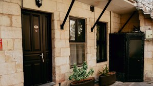 A building facade with a black door, a window, and a black gate. There are two potted plants in front. - Arifbey Konagi Otel (Gaziantep)