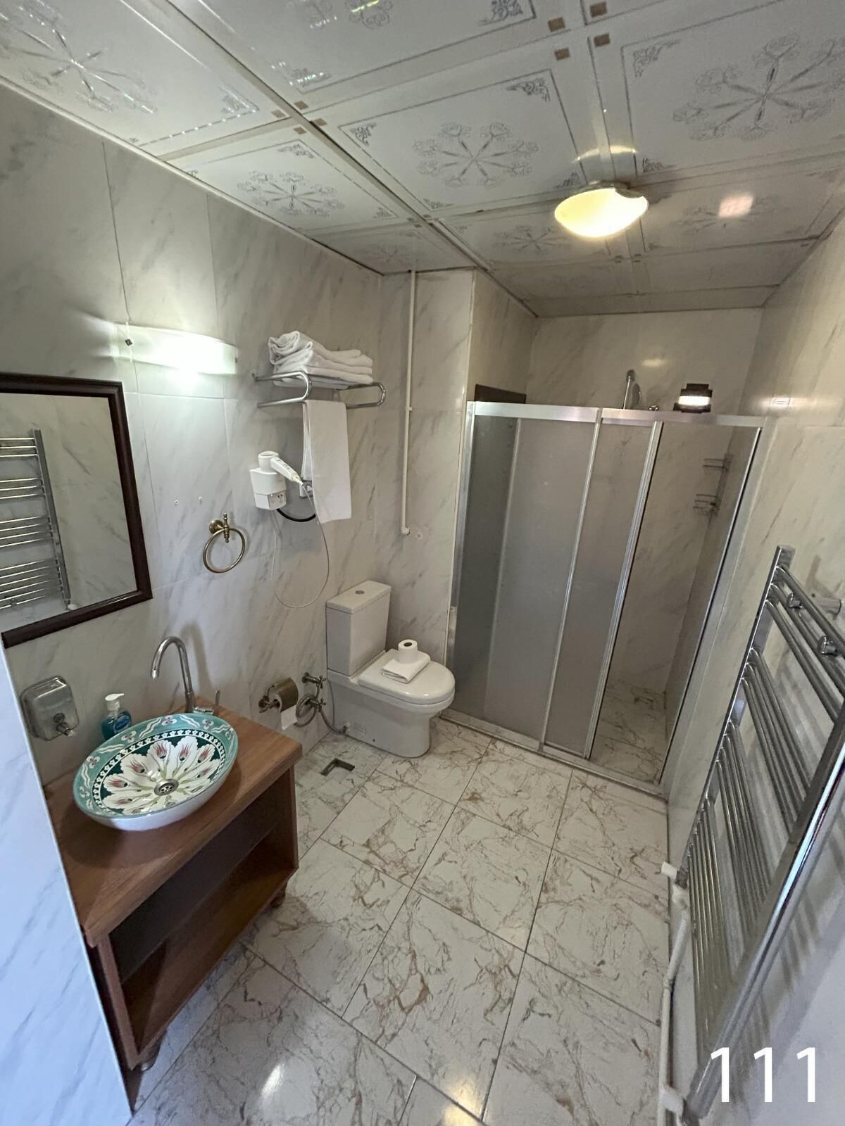 A bathroom with a marble floor, a sink with a floral bowl, a toilet, and a shower enclosure.