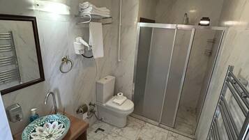 A bathroom with a marble floor, a sink with a floral bowl, a toilet, and a shower enclosure.