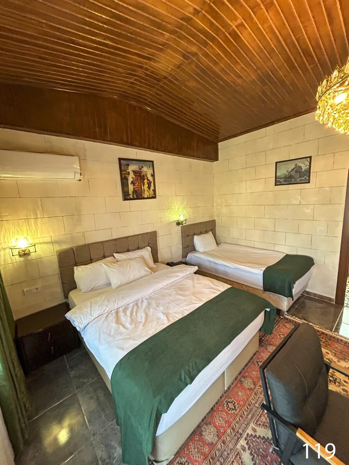 Quarto com duas camas, teto de madeira, paredes de tijolo branco e tapete estampado.
