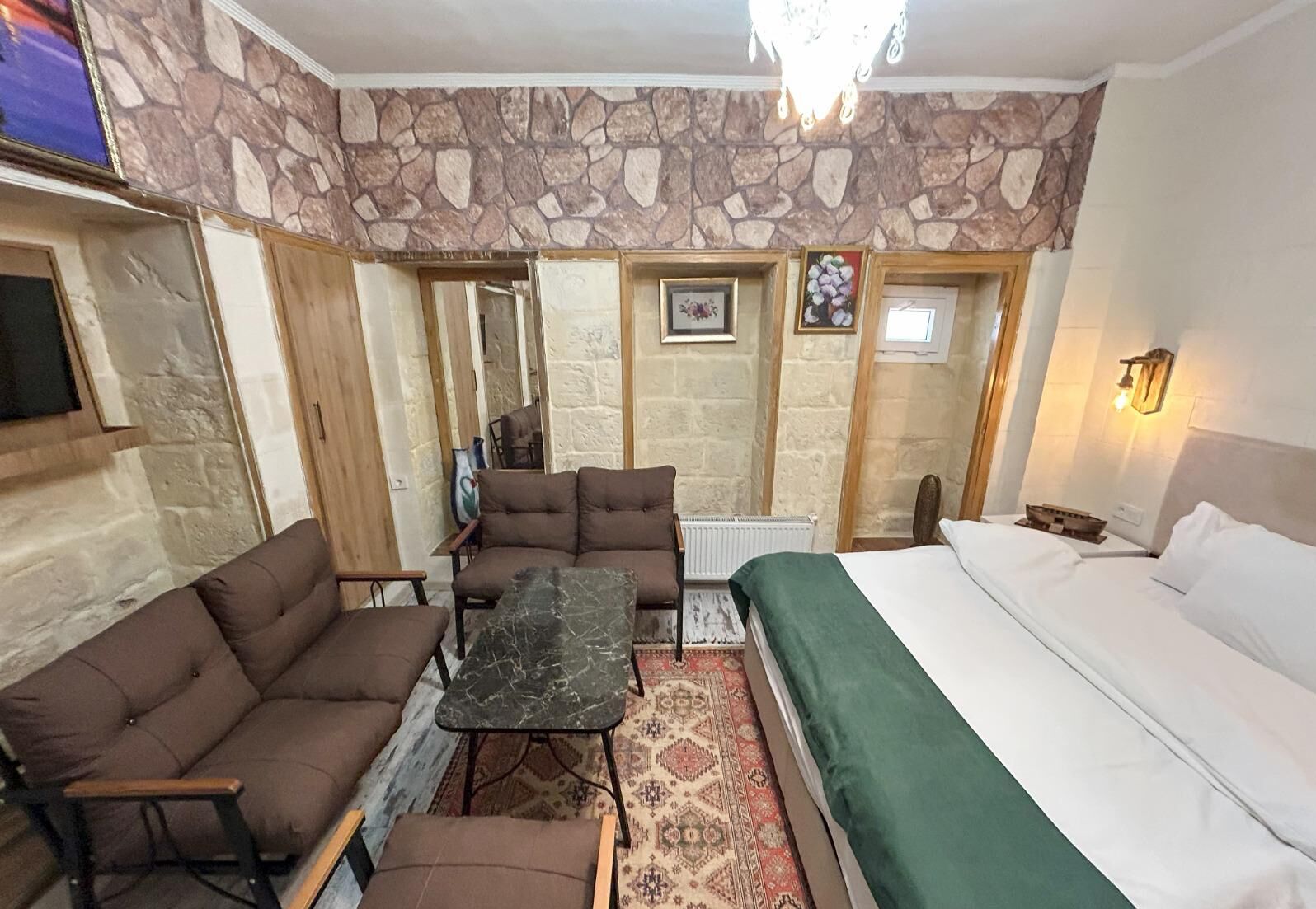 A cozy room with a bed, two sofas, a small table, and a stone wall.