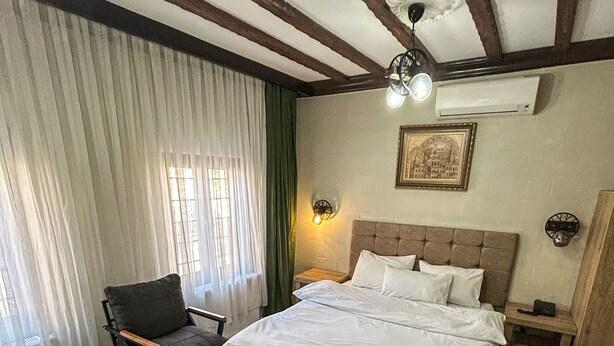 A bedroom with a large bed, a chair, a small table, and a patterned rug. - Arifbey Konagi Otel (Gaziantep)