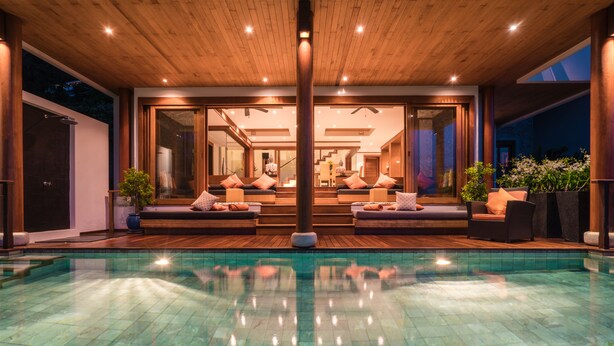 A modern outdoor pool area with a wooden deck, glass doors leading to a living space, and a clear blue pool. - Villa Malisa (Choeng Thale)