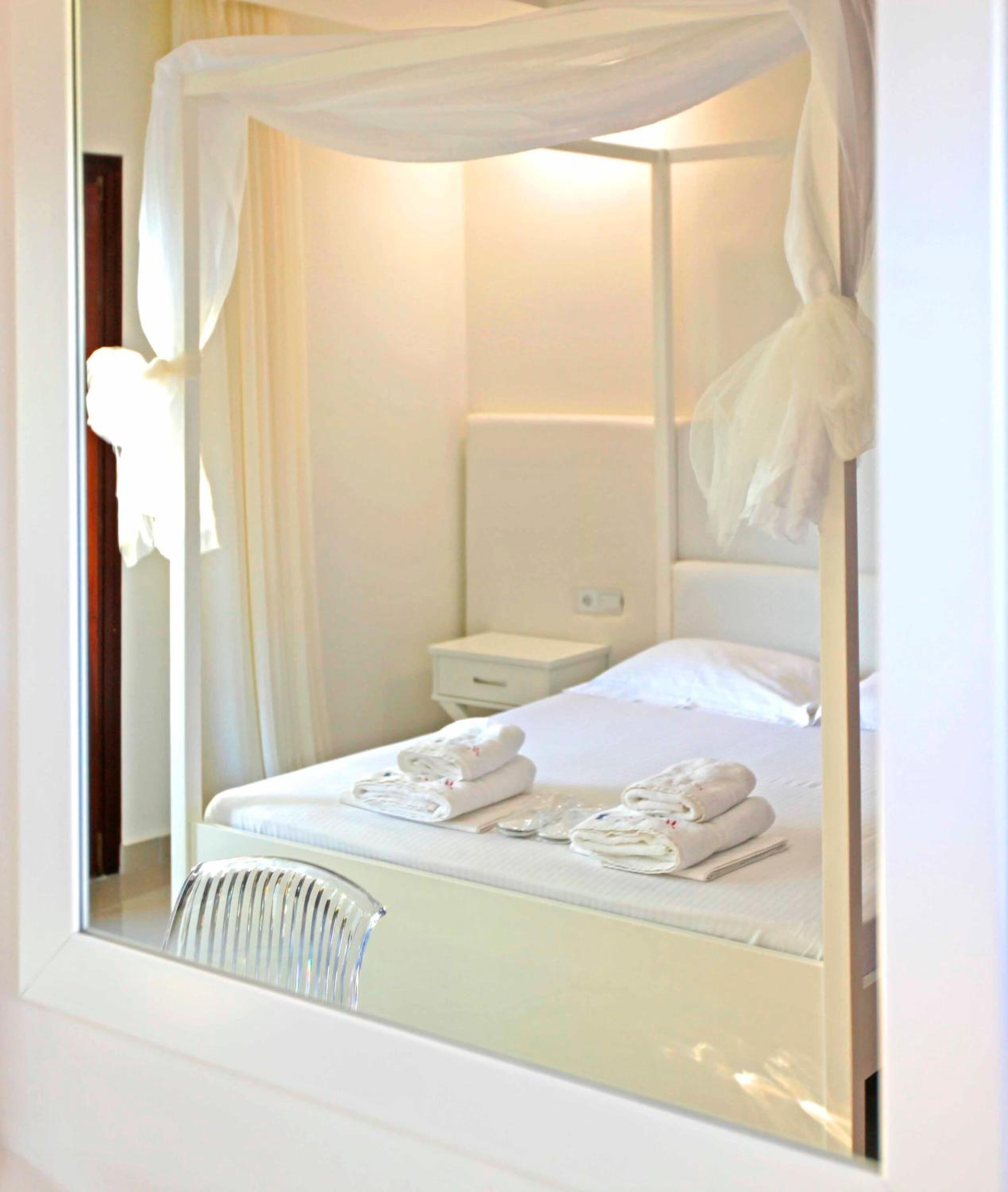 Habitación de hotel con cama a dosel, una mesita de noche y un espejo que refleja la habitación.