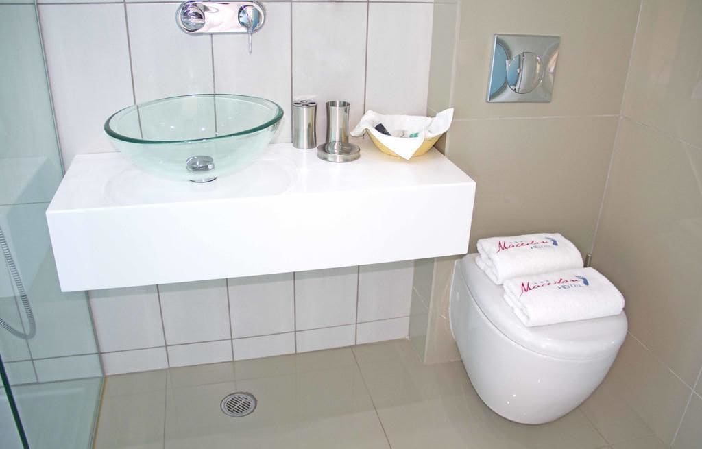 A bathroom with a glass bowl sink, a toilet, and a towel dispenser.