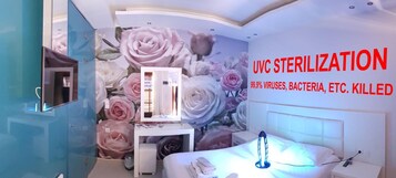 Habitación de hotel con un amplio mural floral, un minibar, una cama con cabecero blanco y un purificador de aire de pared.