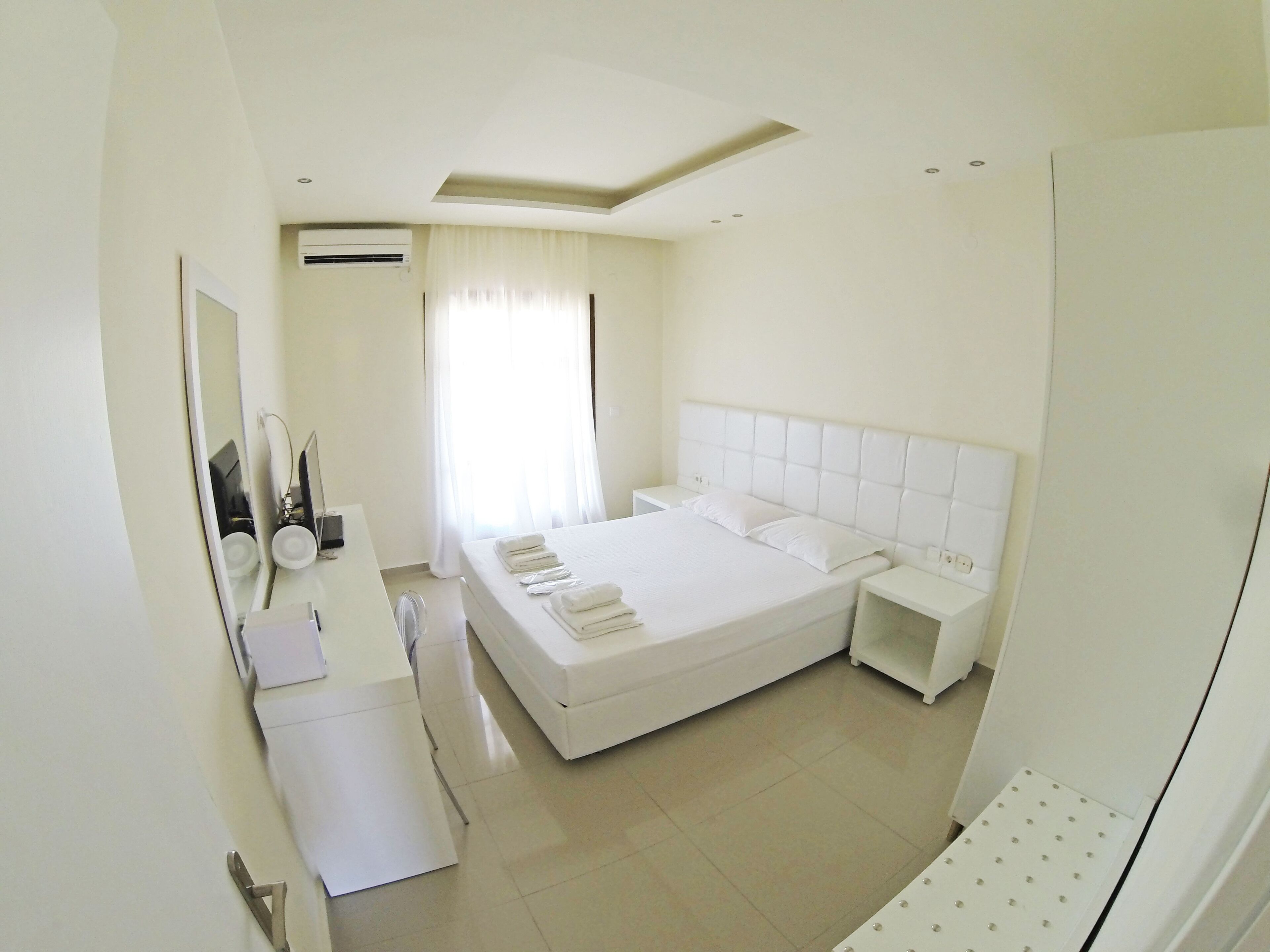 Un dormitorio moderno con una cama grande, mesitas de noche, un espejo y un ventilador de techo.