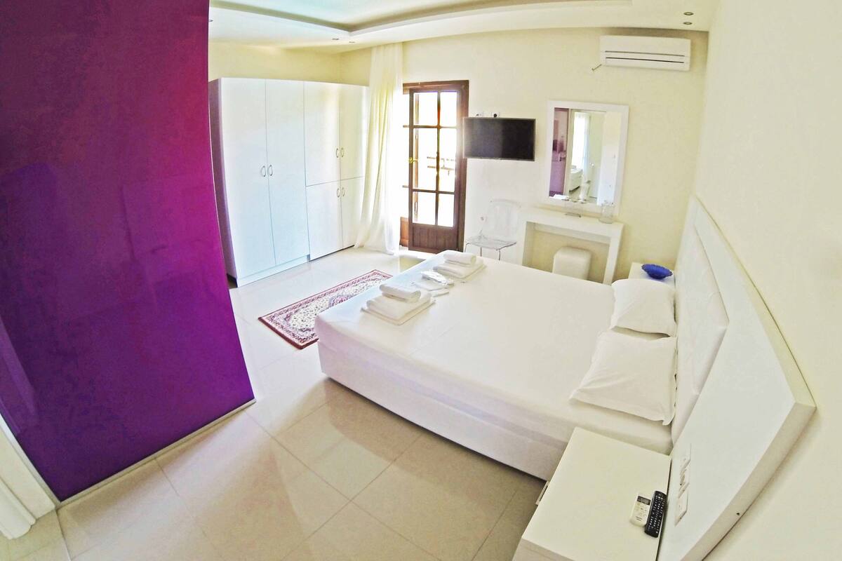 A hotel room with a bed, a desk, a chair, a wardrobe, and an air conditioning unit.