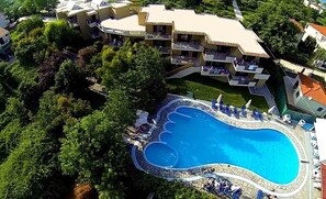 An aerial view of a resort with a large swimming pool surrounded by lush greenery and a multi-story building with balconies. - Hotel Macedon (Thasos)