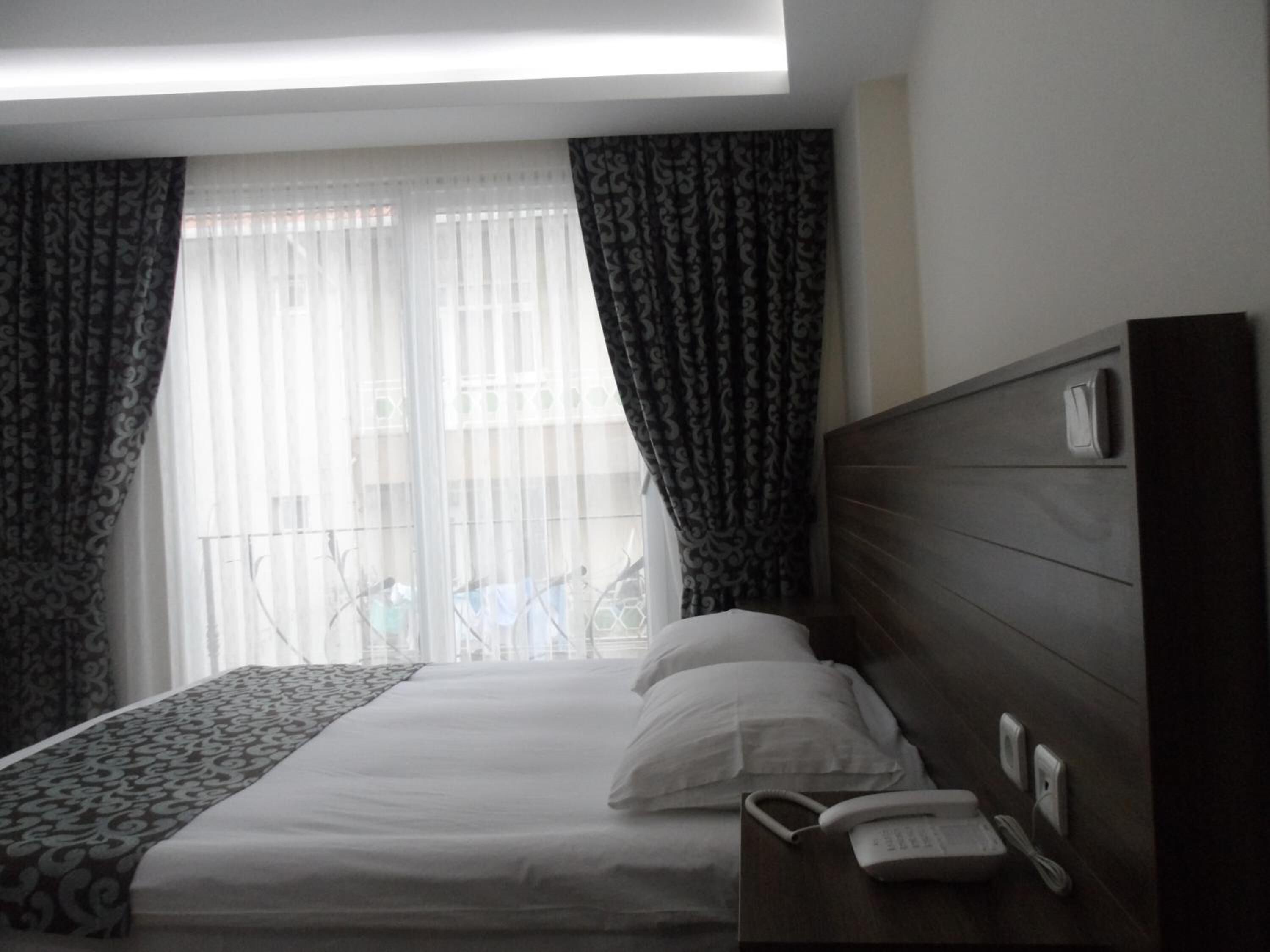 Una habitación de hotel con una cama, un teléfono junto a la cama y una ventana con cortinas.