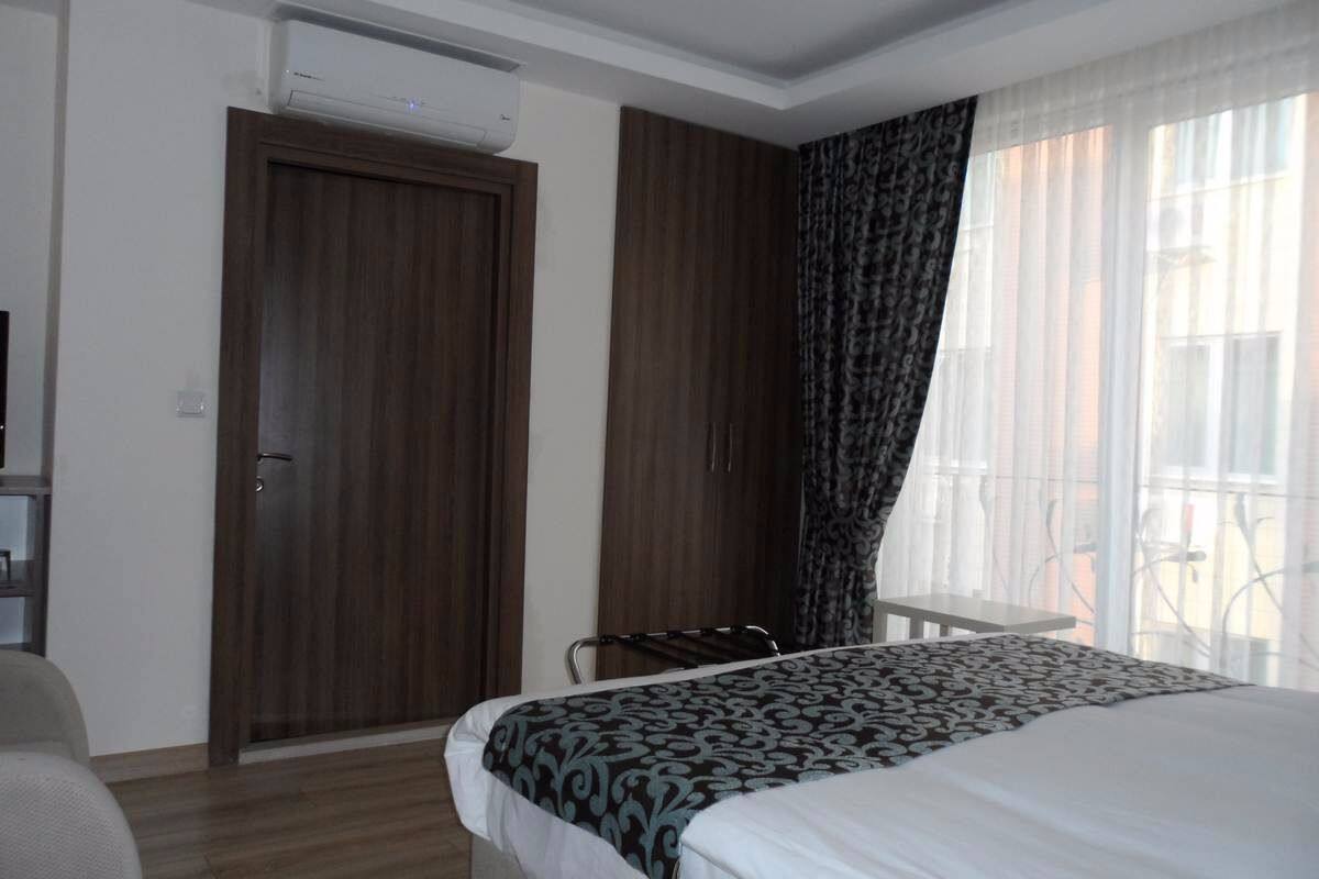 Habitación de hotel con cama, escritorio, silla, equipo de aire acondicionado y ventana con cortinas.
