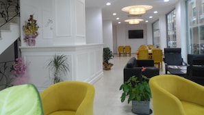 A modern hotel lobby with a white reception desk, yellow chairs, and a large window offering a view of the city. - Zen Inn Boutique (Sarkoy)