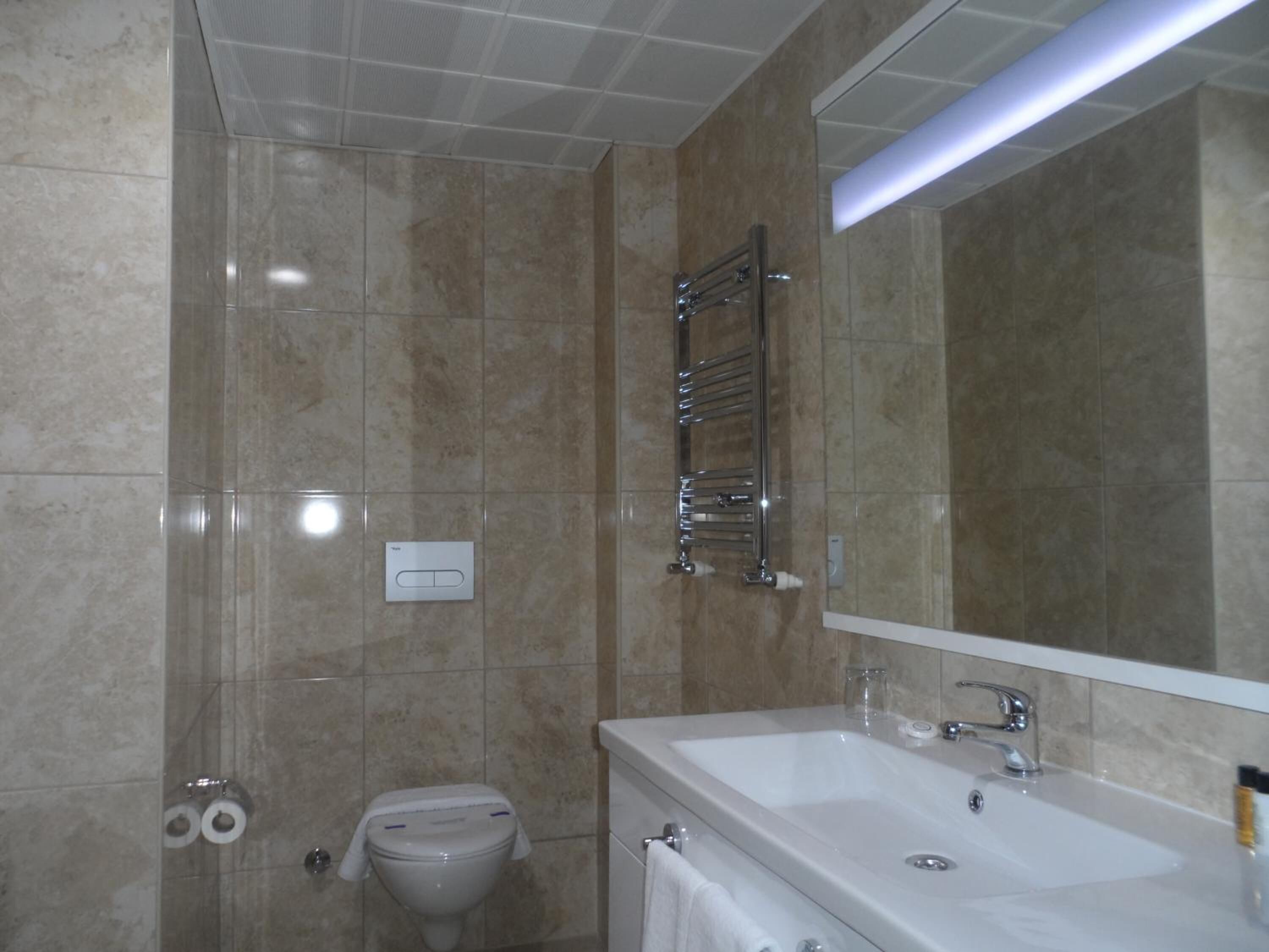 Un baño moderno con un espejo grande, dos lavamanos, un inodoro y un perchero para toallas.