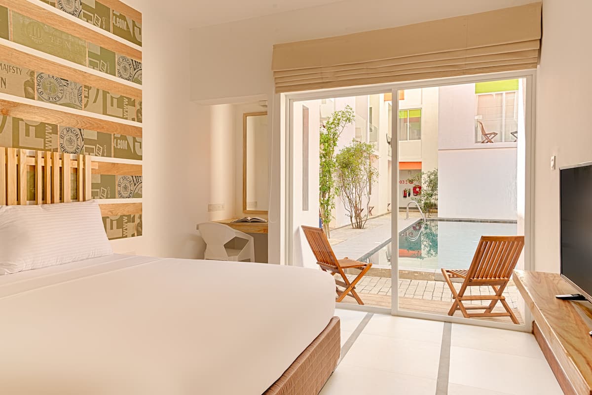 Habitación de hotel con cama, escritorio, silla, televisor y vista a una piscina y zona exterior.